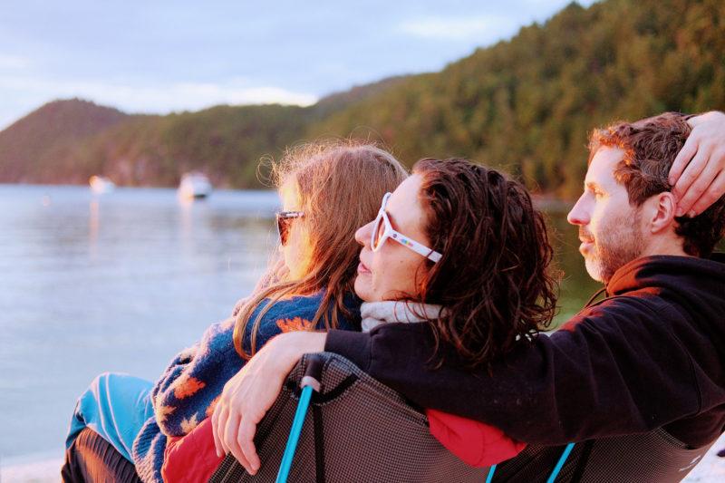 A photo of a family of three sitting by the water.